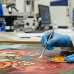 A conservator examines a historical painting in a lab