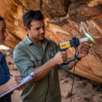 Two archaeologists analyze ancient rock art pigments in a cave.